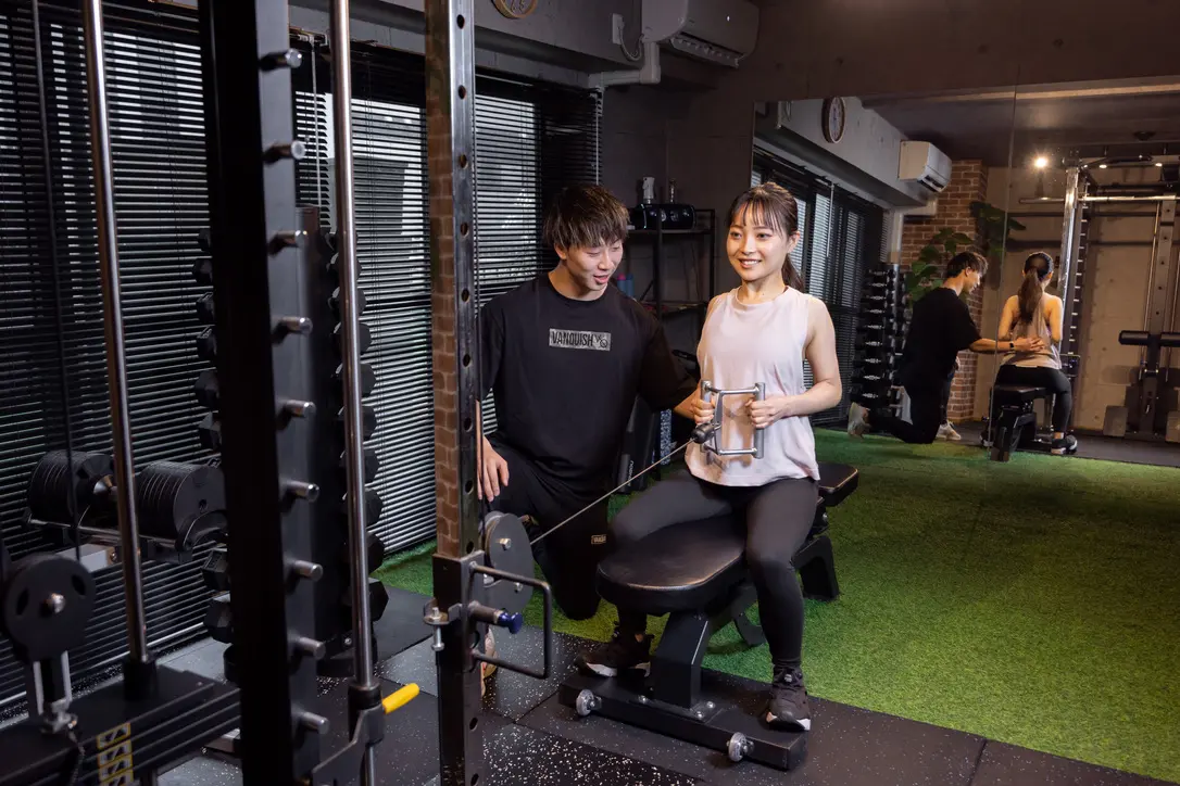 トレーナーがクライアントのケーブルマシンの動作をサポートしている様子